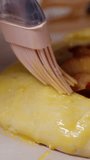 Vertical video. The edges of the peach pie crust are brushed with a brush to create a golden crust.
