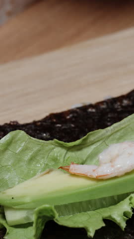 Vertical video. Shrimp is placed on slices of avocado and cucumber to make sushi rolls during the preparation.