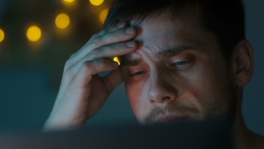 Handsome person suffering from headache at night, holding on head your hand. European businessman working late overtime with laptop at night while feeling exhausted, stress. man massages his temples
