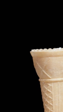 Vertical video. A woman places a scoop of pink ice cream into a waffle cone, on a black background. Isolated.