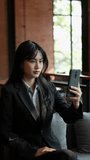 The young Asian businesswoman is having a video call on her smartphone discussing her project over the phone at the coffee shop.