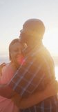 Vertical video of happy senior african american couple embracing on sunny beach. spending free time at beach holiday.