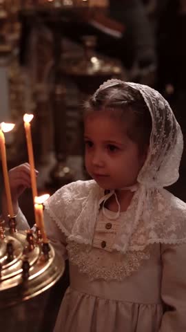a small child girl in a temple or church crosses herself in front of candles and an icon and prays, closing her eyes, asking God to introduce children to church culture Royalty-Free Stock Footage #3470246329