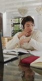 Vertical video of asian male teenager using laptop in living room. spending time alone at home.