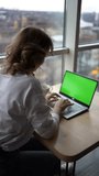 young adult  woman working on a laptop in a coworking space with panoramic windows and a view of the city from above, laptop with a green screen, Chroma key                            