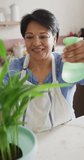 Vertical video of smiling senior biracial woman wearing apron and gardening in kitchen. healthy and active retirement at home.