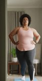Vertical video of plus size biracial woman exercising at home. spending active time at home and body inclusivity.