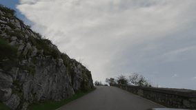 First person view, FPV, from dashcam of car driving winding, high, narrow mountain road to the Covadonga Lakes in Cantabria, Northern Spain, Europe. Road trip video in POV, with clouds and blue sky