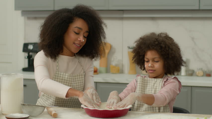 Loving happy African American mom teaching cute kid daughter learning kneading dough funny family child girl helping mother preparing cookies cooking baking pastry knead flour having fun at kitchen Royalty-Free Stock Footage #3470410803