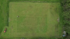 football pitch cutting machine aerial video real time, cutting green grass on a football field,sport concept,Person with pruner cutting the grass inside a football stadium with a tractor

