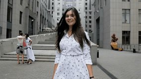 Slow motion video of smiling beautiful woman with long dark hair walking on modern street