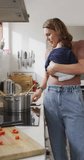 Vertical video of caucasian mother with newborn baby in carrier using smartphone in kitchen. motherhood, parental love and taking care of newborn baby concept digitally generated video.