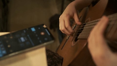 A teenage girl learns to play the classical guitar at home, with a phone, a program for musicians. Home education , skill, homework. Top view, close up 4 kの動画素材