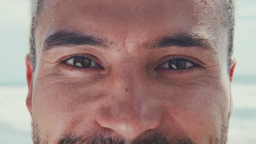 Portrait of Young Caucasian Man Looking at Camera Closeup. Cute Smiling Face and Beautiful Dark Eyes of Happy Male Person Posing Outdoors. Close-Up Crop Shot of Funny Adult Boy with Amazing Wellness
