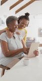 Vertical video of happy senior african american woman using tablet with adult daughter at home. senior healthcare and medical physiotherapy treatment.