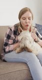 Vertical video of happy caucasian woman petting her dog at home. spending time together at home.