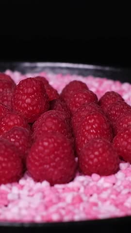 Close-up of fresh juicy raspberries and little, raspberry flavoured candy pieces rotating on a plate. Healthy organic red fruits versus unhealthy sweets. Cake topping, vegetarian or vegan diet concept
