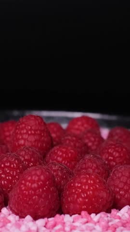 Close-up of fresh juicy raspberries and little, raspberry flavoured candy pieces rotating on a plate. Healthy organic red fruits versus unhealthy sweets. Cake topping, vegetarian or vegan diet concept