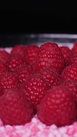 Close-up of fresh juicy raspberries and little, raspberry flavoured candy pieces rotating on a plate. Healthy organic red fruits versus unhealthy sweets. Cake topping, vegetarian or vegan diet concept
