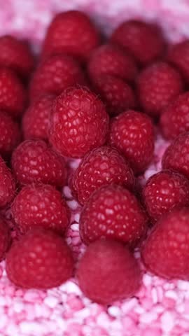 Close-up of fresh juicy raspberries and little, raspberry flavoured candy pieces rotating on a plate. Healthy organic red fruits versus unhealthy sweets. Cake topping, vegetarian or vegan diet concept