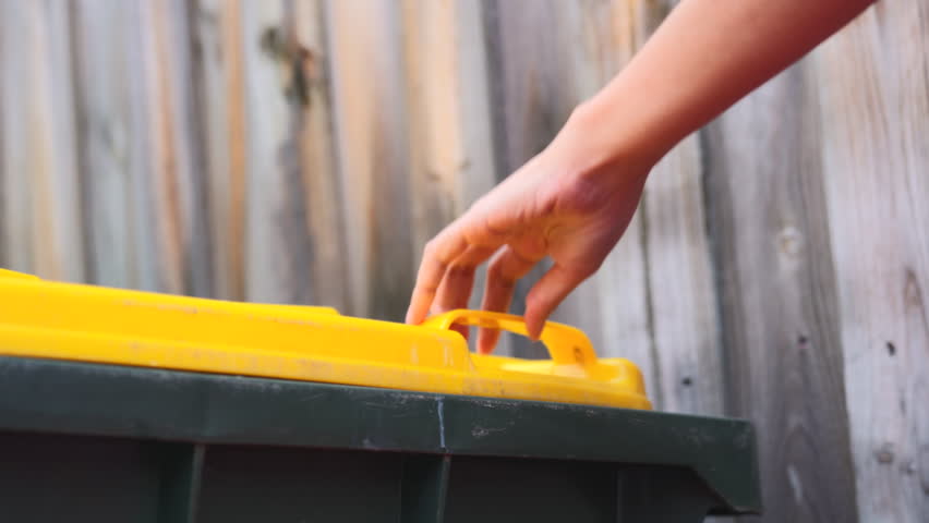 Waste Recycling Concept. Unrecognizable lady throwing plastic bottle into yellow recycle bin container outdoors, sorting garbage, enjoying zero waste living, cropped image with selective focus.