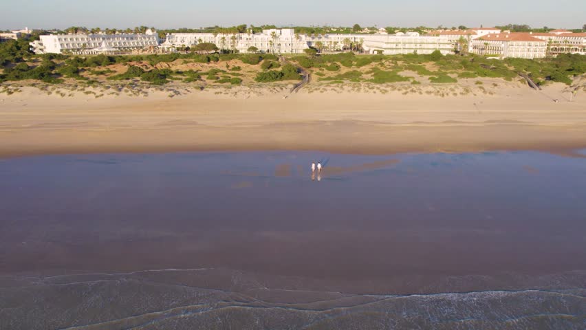  Aerial view of a silholouette of a romantic couple relaxing enjoying on beach with beautiful light and colors. Young couple on honeymoon enjoying travel vacation summer holidays on beach. Slow motion