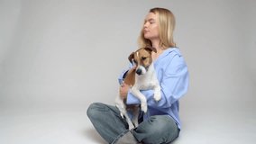 Blonde woman in blue shirt petting cute relaxed sleepy white dog. Friends trust and love. Dog owner studio video footage grey background
