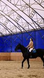 Long-haired woman riding a beautiful black horse. Female lady coach walks in front of animal. Young girl comes up to the foreground. Vertical video