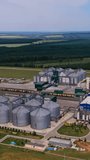 Industrial plant territory for storage grain. Silver tanks and other plant premises exterior from aerial perspective. Nature landscape at the backdrop. Vertical video