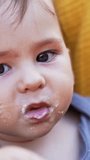 Nice Caucasian toddler eating porridge willingly. Portrait of a baby with porridge on his face looking at camera. Close up. Vertical video