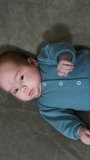 Beautiful toddler kid in blue suit on the bed. Baby boy lying peacefully on grey background. View from above. Vertical video