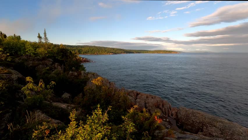 View of lake and coast at sunset under partly cloudy sky, at north shore of Lake Superior, Ontario, Canada.