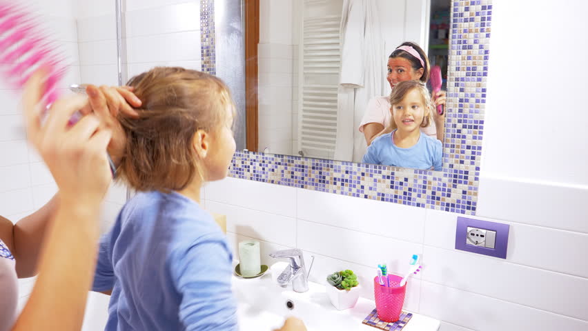 Happy mother and little daughter having fun in bathroom in front of mirror