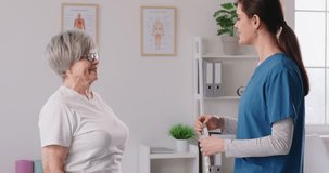Health monitoring. Young nurse measuring elderly female patient's waistline during medical examination. In hospital room, nurse carefully explains process and has casual conversation with older woman