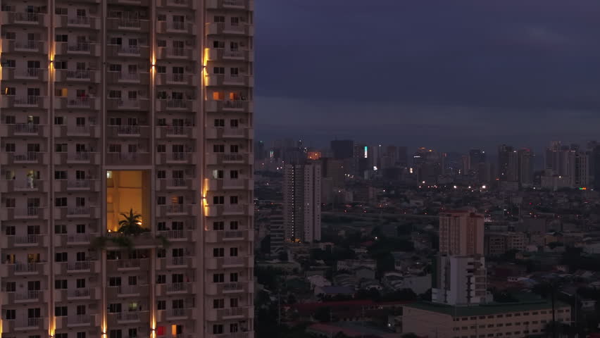 Modern high rise apartment building with balconies and panoramic view of evening city in background. Manila, Philippines
