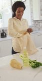 Vertical video of happy african american woman unpacking groceries in kitchen. cooking, lifestyle and spending time at home.