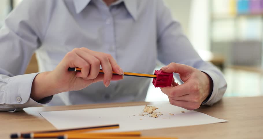 Closeup of woman hands sharpening a pencil with red sharpener at the workplace. Secretary preparing pencils