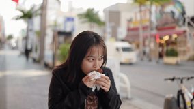 Slow-motion video of Okinawan women in their 20s in winter clothes eating street food on Kokusai Street in Naha City, Okinawa Prefecture