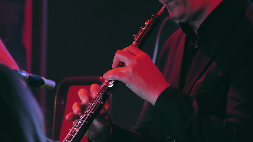 A close-up of a man playing the clarinet in an orchestra. A concert venue with musicians on a dimly lit stage. A symphony orchestra