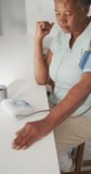 Vertical video of senior african american woman measuring pressure at home. senior healthcare and medical physiotherapy treatment.