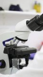 Vertical videos of a Mature male lab technician observing a sample through a microscope, ready to analyze a test tube in a well-equipped scientific research laboratory