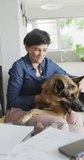 Vertical video of happy caucasian woman petting her dog at home. spending time together at home.