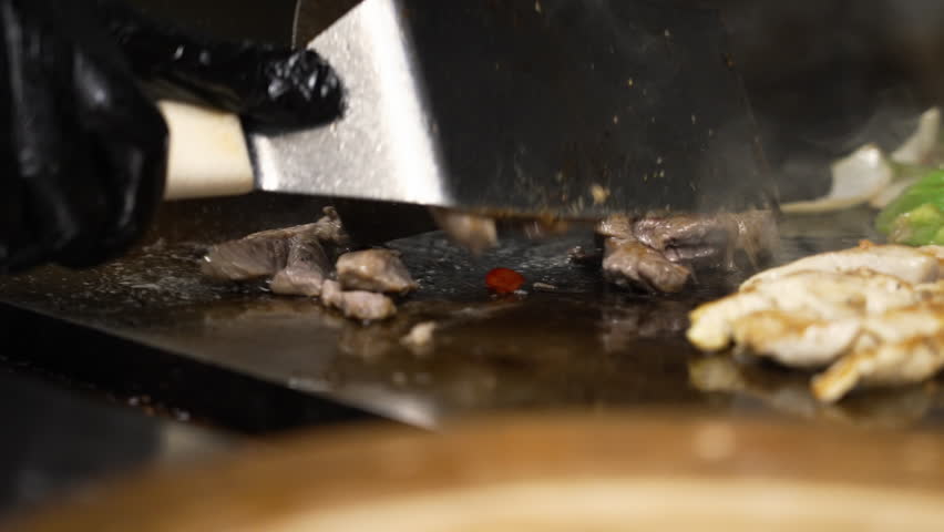 Spatula flips sizzling beef fajita strips on flat top grill, chicken and beef fajitas with peppers and onions cooking in commercial restaurant kitchen griddle, slow motion close up 4K Royalty-Free Stock Footage #3471438727
