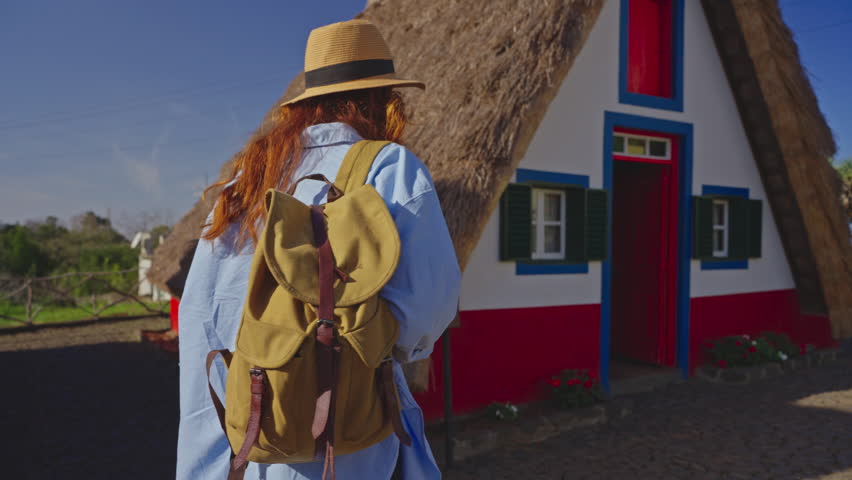 A girl travels in a hat and with a backpack and visits extraordinary traditional A-shaped houses in Santana in Portugal Madeira