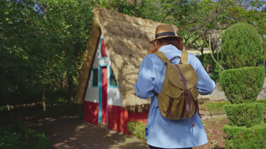 A girl travels in a hat and with a backpack and visits extraordinary traditional A-shaped houses in Santana in Portugal Madeira