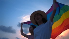 Happy lesbian couple walking and waving lgbt flag on sunset light in beautiful beach. Happy asian lesbian woman demonstrate their rights. LGBTQI, Pride Event, LGBT Pride Month, Gay Pride Symbol - Powered by Shutterstock - Get 15% off with code: PIKWIZARD15