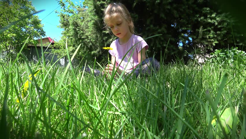a little girl sits in the grass and looks at a flower