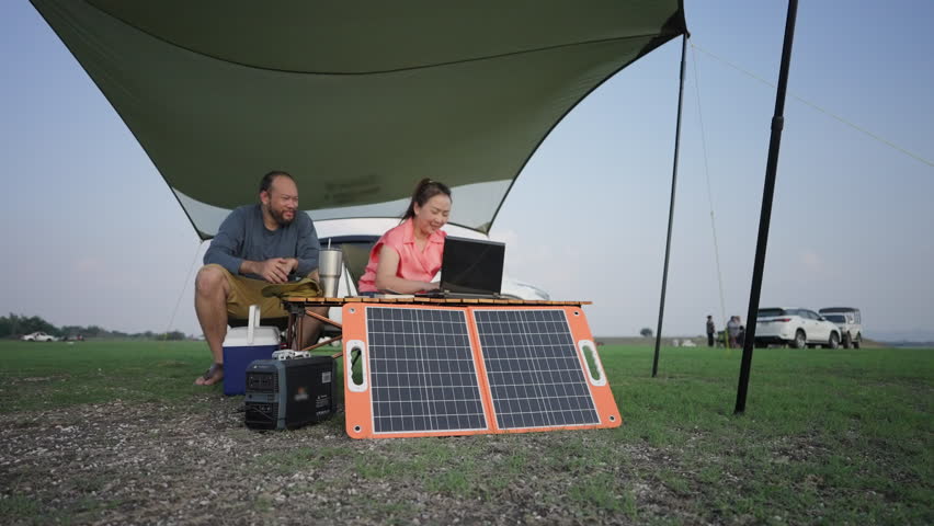 Asian woman working on laptop powered by a portable solar panel or solar cells in an outdoor setting, embodying sustainable energy use and mobile office concepts