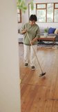 Vertical video of senior biracial woman cleaning floor in living room. healthy and active retirement at home.