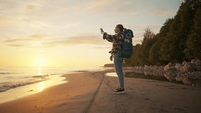 Woman tourist takes photo of sea sunset. Female hiker camper with touristic backpack recording video of nature on smartphone enjoying vacations. Travel tourism admire hike camping wanderlust concept.